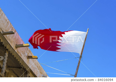 National flag of Qatar on a flagpole in front of blue sky National flag of Qatar on a flagpole in front of blue sky 84016094