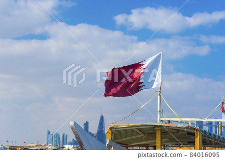 National flag of Qatar on a flagpole in front of blue sky National flag of Qatar on a flagpole in front of blue sky 84016095
