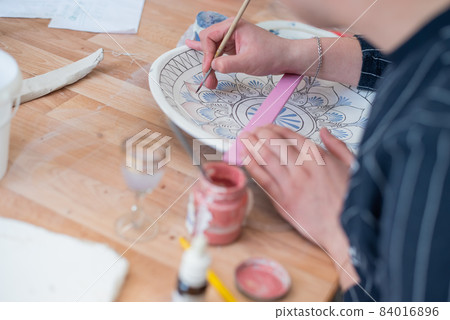 A young man painting a ceramic plate. 84016896