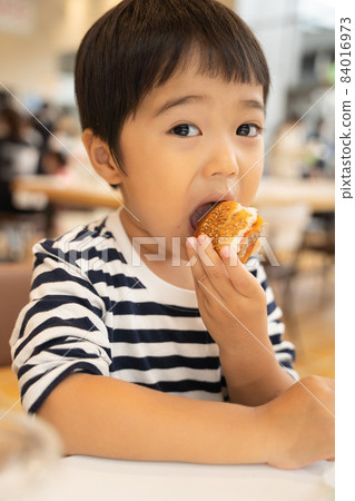 4-year-old boy eating a hamburger at the food court 84016973