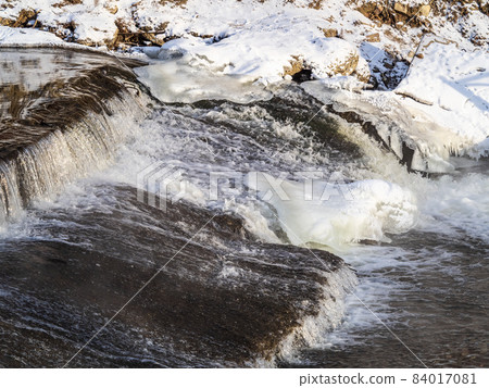 A stream of water flows among ice and snow. 84017081