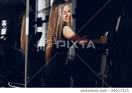 Attractive young blonde woman exercising on cardio training apparatus 84017125