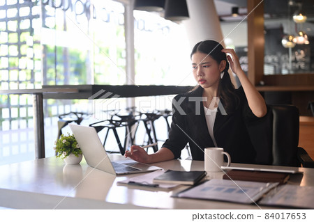 Confused businesswoman analyzing financial information on laptop computer. 84017653