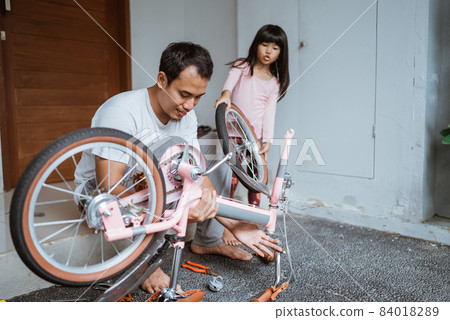 Asian father holding bicycle frame and daughter carrying wheels 84018289