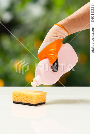 Man's hand in protective glove with bottle of dishwashing liquid. Man's hand in protective glove with bottle of dishwashing liquid. 84018338