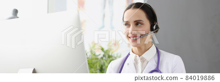Doctor in headphones with microphone holding x ray in front of computer screen 84019886