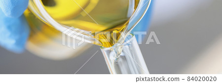 Scientist chemist pouring yellow oil from glass jar into test tube closeup 84020020