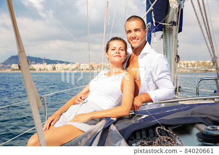 Young woman and man sitting on modern yacht deck, enjoying warm summer day during romantic sea travel 84020661