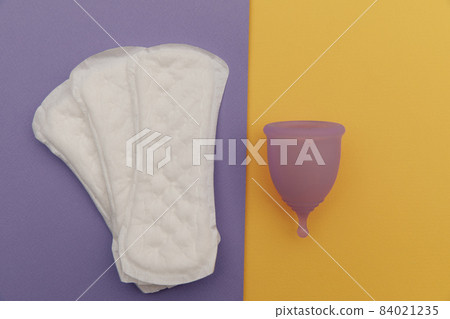 Purple menstrual cup and pads on a colorful background. Ways of women's hygiene 84021235