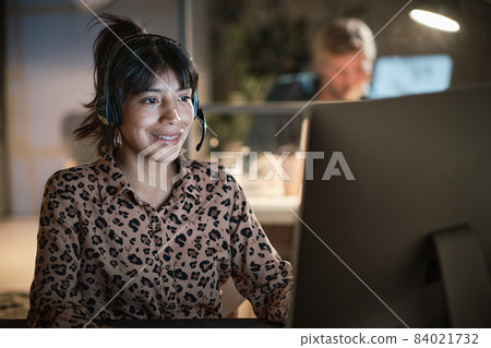 Young smiling businesswoman sitting at desk, making a call, using headset and laptop Young smiling businesswoman sitting at desk, making a call, using headset and laptop 84021732