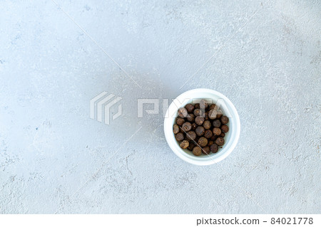 Whole dried black peppercorns in a round white bowl on a gray background 84021778