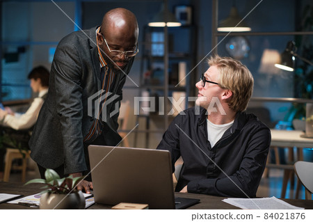 Businessman sitting at the table with laptop discusing online work together with his colleague during their work at office 84021876