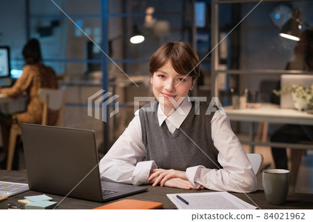 Portrait of young businesswoman sitting at the table with laptop and smiling at camera during her work at office Portrait of young businesswoman sitting at the table with laptop and smiling at camera during her work at office 84021962
