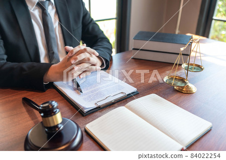 Justice concept an honorable judge sitting at the middle of the big wooden table with the judging hammer and the libra looking powerful 84022254