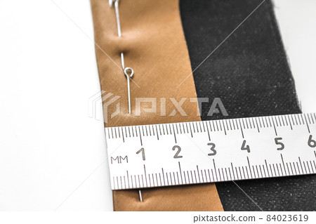 Processing of the seam with an oblique brown silk label. Close-up, wrong side. The seam is pinned with pins, the process of measuring the width of the seam. Concept: atelier, sewing hobby. Processing of the seam with an oblique brown silk label. Close-up, wrong side. The seam is pinned with pins, the process of measuring the width of the seam. Concept: atelier, sewing hobby. 84023619