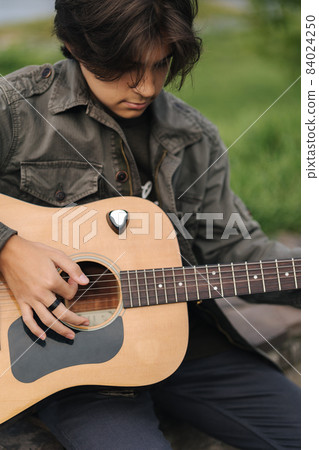 Portrait of handsome teenage boy playing guitar outdoor. Boy using classic guitar. Male alone making music 84024250