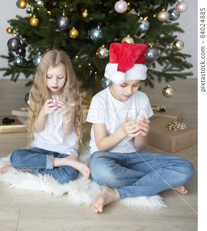 Children - a boy and a girl are playing near the Christmas tree. Children - a boy and a girl are playing near the Christmas tree. 84024885