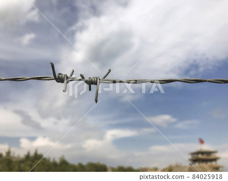 barbed wire against blue sky and defocused building 84025918