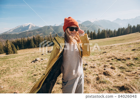 Young blond woman with sunglasses dancing in mountains. Freedom, happiness, travel and vacations concept, outdoor activities. Happy Girl wearing red hat and a yellow jacket Young blond woman with sunglasses dancing in mountains. Freedom, happiness, travel and vacations concept, outdoor activities. Happy Girl wearing red hat and a yellow jacket 84026048
