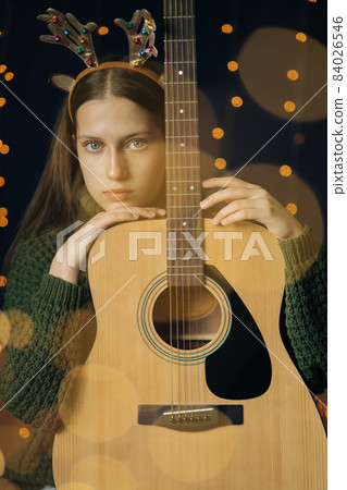 Beautiful teenage girl in Christmas antlers and a green sweater with guitar 84026546