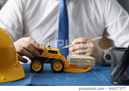 Yellow miniature toy excavator on blueprint carry wooden blocks Yellow miniature toy excavator on blueprint carry wooden blocks 84027577