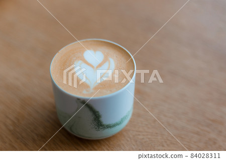 One Cup of cappuccino with latte art. Coffee in white cup on brown wooden table in cafe. Concept of easy breakfast. One Cup of cappuccino with latte art. Coffee in white cup on brown wooden table in cafe. Concept of easy breakfast. 84028311