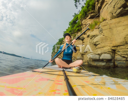 Young women Having Fun Stand Up Paddling in the sea. SUP. Red hair girl Training on Paddle Board near the rocks 84028485