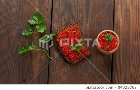 red salmon caviar lies on a piece of rye bread. Brown wooden table red salmon caviar lies on a piece of rye bread. Brown wooden table 84028762