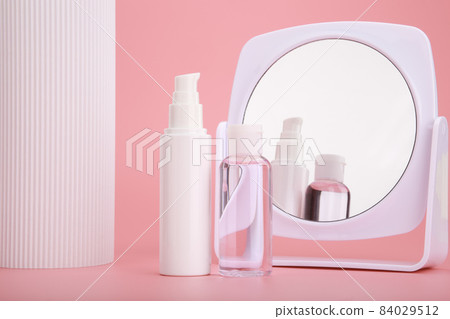 Set of two cosmetic bottles next to white column and mirror against bright pink background  84029512