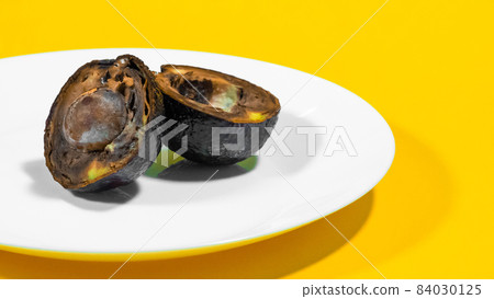 An avocado cut in half moldy on a plate Yellow background Rotten Food Contaminated Avocado Necomestibile Fruits Wasting Food Unhealthy Tropical Fruits. Food Concept. Copy space. 84030125