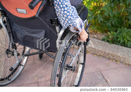 Asian middle-aged lady woman patient sitting on wheelchair in park; healthy strong medical concept 84030965