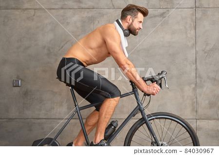 Athletic young man riding stationery bike against the wall 84030967