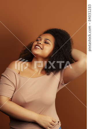 pretty young african american woman with curly hair posing cheerful gesturing on brown background, lifestyle people concept 84031283