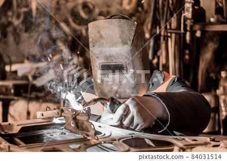 A welder worker in a protective metal mask is engaged in welding and repair of a car door, metal work in the workshop of the plant A welder worker in a protective metal mask is engaged in welding and repair of a car door, metal work in the workshop of the plant 84031514
