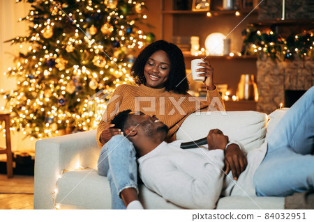Lovely black woman spending time with her happy boyfriend on Christmas eve in decorated living room, copy space Lovely black woman spending time with her happy boyfriend on Christmas eve in decorated living room, copy space 84032951
