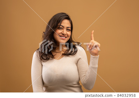 Portrait of positive arab lady pointing finger up at copy space and smiling at camera over brown studio background 84032958