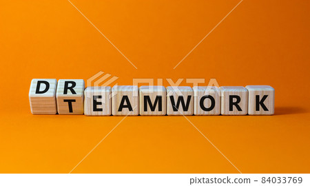 Teamwork and dream work symbol. Turned wooden cubes and changed the word 'dreamwork' to 'teamwork'. Beautiful orange background. Business, teamwork and dream work concept, copy space. 84033769