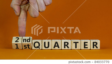 From 1st to 2nd quater symbol. Businessman turns cubes and changes words '1st quater' to '2nd quater'. Beautiful orange table, orange background. Business, happy 2nd quater concept, copy space. 84033770
