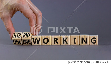 Hybrid or online working symbol. Businessman turns cubes and changes words 'online working' to 'hybrid working'. Beautiful grey background. Business, hybrid or online working concept, copy space. 84033771