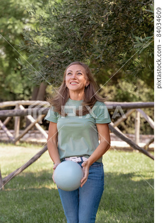 Women wearing t-shirt and jeans plays with ball in park 84034609