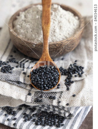 Bowl with a spoon of black lentils flour and beans on white wooden table close up 84034613