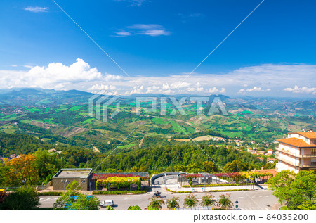 Aerial top panoramic view of landscape with valley, green hills, fields and villages of Republic San Marino 84035200