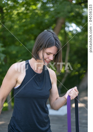 Fitness woman doing exercise for biceps with resistance band outdoors. Athletic girl workout. Close up Fitness woman doing exercise for biceps with resistance band outdoors. Athletic girl workout. Close up 84036183