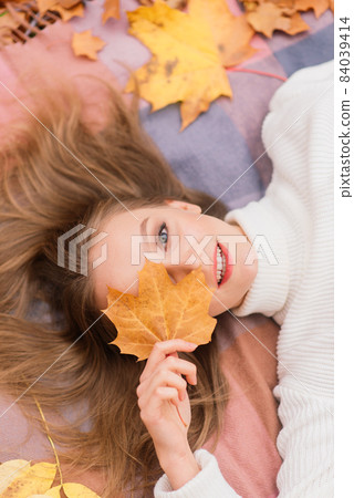 Season and people concept - beautiful young woman with autumn maple leaves lying on ground 84039414