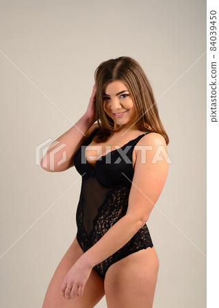 Beautiful emotional plus-size female model in pink and black bodysuit posing on background in studio 84039450