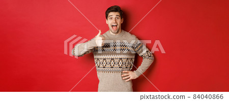 Portrait of excited, attractive man in christmas sweater, showing thumbs-up and looking amazed, recommending good thing, advertising christmas related product 84040866