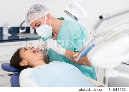 Dentist man examining a latin female patient teeth Dentist man examining a latin female patient teeth 84048262