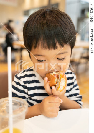 4-year-old child chewing on a hamburger at the food court 84048509