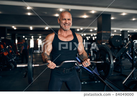 Muscular bald man working out in gym doing exercises with barbell at biceps. Bodybuilding concept 84049000