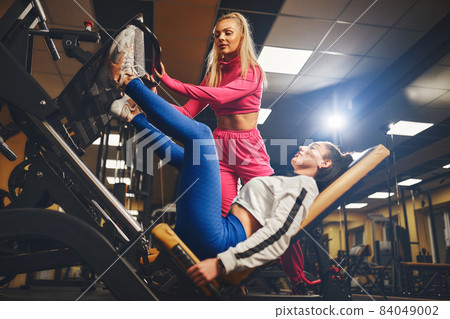Personal trainer helping woman in works out on training apparatus inside in fitness center. Sporty lifestyle, bodybuilding, training concept Personal trainer helping woman in works out on training apparatus inside in fitness center. Sporty lifestyle, bodybuilding, training concept 84049002